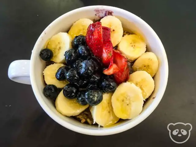 Acai bowl in a mug, topped with blueberries, sliced strawberries and bananas.
