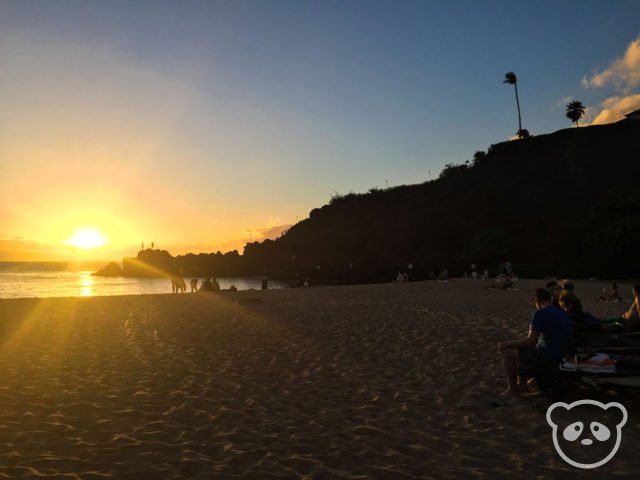 Sunset from the beach with people atop of Black Rock ready to cliff dive.