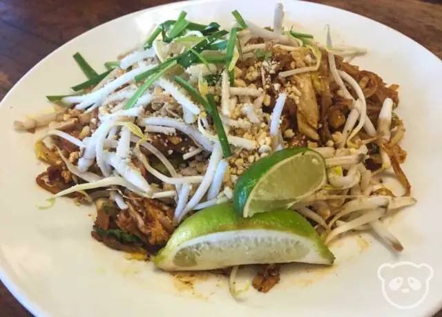 Stir fried noodle dish with bean sprouts and limes on the side.